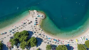 Luftaufnahme eines belebten Sandstrandes mit klarem türkisfarbenem Wasser und vielen Sonnenanbetern.