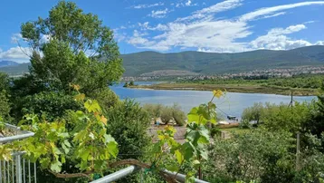 Blick vom Balkon auf den See, umgeben von grüner Landschaft und Bergen unter blauem Himmel.