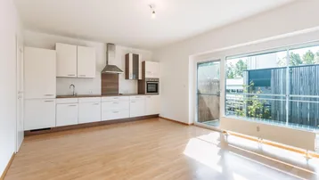 Moderne Einbauküche mit weißen Schränken und Holzakzenten, offen zum hellen Wohnbereich mit Balkonzugang.