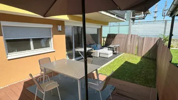 Gemütliche Terrasse mit Sitzgelegenheiten, Sonnenschirm und angrenzendem kleinen Gartenbereich.