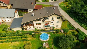 Luftaufnahme eines Hauses mit Garten, kleinem Pool und angrenzendem Weinberg in grüner Umgebung.