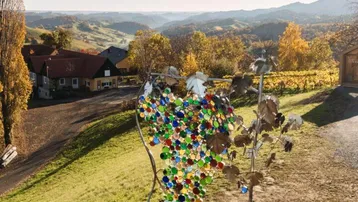 Kunstinstallation in Form einer Weintraube mit bunten Glasstücken vor einer malerischen Weinlandschaft.