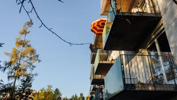 Blick auf die Balkone eines Mehrfamilienhauses mit Bäumen im Hintergrund.
