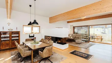 Geräumiger offener Wohn- und Essbereich mit Holzbalken, Kamin und Zugang zum Balkon.