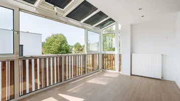 Heller Wintergarten mit großen Fenstern, Laminatboden und weitem Blick ins Grüne.