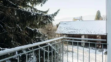 Kleiner Balkon mit Metallgeländer und Blick auf verschneite Bäume und ein Nebengebäude.