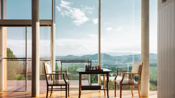 Helles Wohnzimmer mit Holzboden, Schachspiel und weitem Blick auf die Landschaft und Berge.