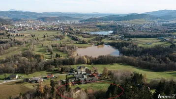 Luftaufnahme einer ländlichen Gegend mit einem See, umgeben von Wäldern und Feldern, mit verstreuten Häusern.