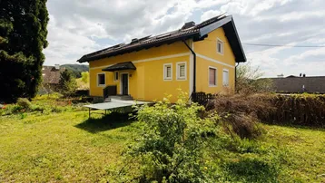 Seitenansicht des gelben Hauses mit großem Garten und einer Tischtennisplatte im Freien.