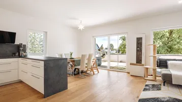 Helles, offenes Wohn-Esszimmer mit moderner Küche, Holzboden und Zugang zur Terrasse.