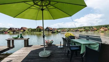 Geräumige Holzterrasse mit Esstisch und Sonnenschirm direkt am See, ideal für Mahlzeiten im Freien.
