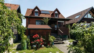 Charmantes Holzhaus mit rotem Ziegeldach, umgeben von einem gepflegten Garten und Sträuchern.
