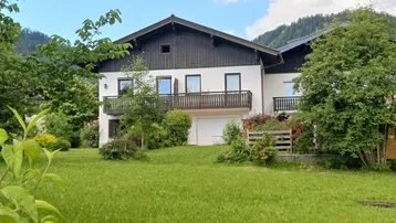 Traditionelles Haus mit weißer Fassade, Holzbalkonen und gepflegtem Garten in alpiner Umgebung.