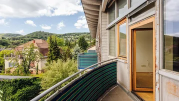 Gebogener Balkon mit Sichtschutz und Panoramablick auf die umliegende grüne Landschaft.