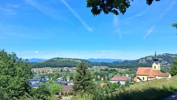 Weitblick über ein malerisches Dorf mit Kirche, umgeben von grünen Hügeln und Bergen.