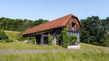 Rustikales Haus mit rotem Ziegeldach und Holzfassade, eingebettet in grüne Landschaft.