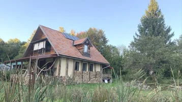 Ländliches Haus mit Holzfassade, Ziegeldach und Solarpaneelen, umgeben von Natur.