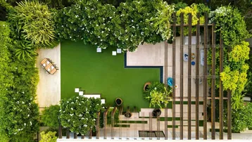 Wunderschöner, modern gestalteter Garten mit großer Rasenfläche, Pergola und gemütlichem Essbereich im Freien.