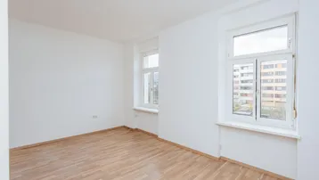 Helles Zimmer mit weiß gestrichenen Wänden und Parkettboden, ideal als Wohn- oder Schlafzimmer.