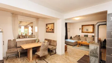 Gemütlicher Wohn-Essbereich mit Holztisch, Eckbank, Sofa und einem Kaminofen.