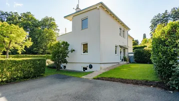 Helles Einfamilienhaus mit gepflegtem Rasen und Zufahrt an einem sonnigen Tag.