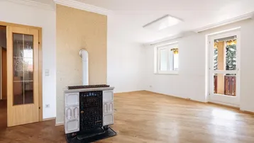 Helles Wohnzimmer mit Holzboden, traditionellem Kachelofen und Zugang zum Balkon.