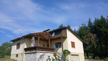 Gesamtansicht des Einfamilienhauses mit Garten und umgebender Natur unter blauem Himmel.