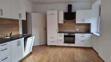 Moderne Einbauküche mit weißen Fronten, Holzoptik-Rückwand und Parkettboden, inklusive Geschirrspüler und Dunstabzugshaube.