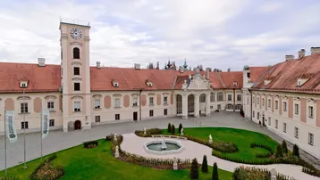 Großzügiger Innenhof eines historischen Gebäudes mit Uhr-Turm, Brunnen und gepflegter Grünfläche.