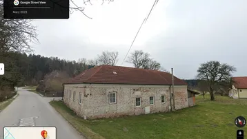 Altes Gebäude mit Ziegeldach und verputzter Backsteinfassade, umgeben von ländlicher Landschaft.