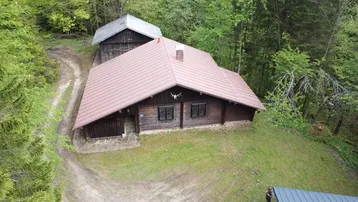 Luftaufnahme einer rustikalen Holzhütte mit rotem Dach, umgeben von dichtem Wald und einem Feldweg.