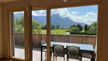 Heller Innenraum mit Holzelementen und großem Fenster, das einen atemberaubenden Blick auf Berge und See bietet.