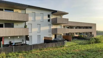 Modernes Mehrfamilienhaus mit Terrassen und Balkonen, umgeben von grüner Landschaft.