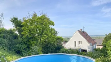 Panoramablick auf den Außenpool mit weitreichender grüner Landschaft und Häusern im Hintergrund.