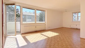 Helles Wohnzimmer mit Parkettboden, großen Fenstern und Zugang zu einem sonnigen Balkon.