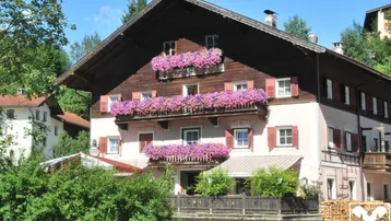 Traditionelles Gebäude mit blumengeschmückten Balkonen und Holzfassade in alpiner Umgebung.