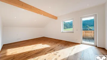 Helles Zimmer im Dachgeschoss mit Holzbalken, Parkettboden und Zugang zu einem Balkon mit Bergblick.