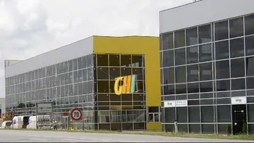 Moderne Gewerbegebäude mit großen Glasfassaden und gelben Akzenten an einer Straße unter bewölktem Himmel.