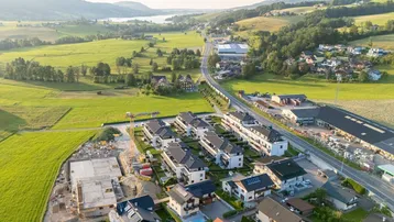 Luftaufnahme einer ländlichen Wohngegend mit Neubauten, einer Straße und einem See am Horizont.