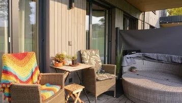 Gemütlicher Balkon mit Holzboden, Rattanmöbeln und farbenfrohen Decken, ideal zum Entspannen.