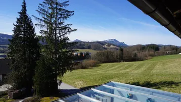 Weitläufiger Blick über grüne Felder und Wälder bis zu den schneebedeckten Bergen am Horizont.