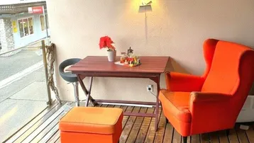 Gemütlicher Balkon mit Holzfußboden, bequemen orangefarbenen Möbeln und Blick auf die Umgebung.