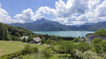 Weitläufiger Blick auf die Berglandschaft mit einem See und mehreren Häusern unter blauem Himmel.