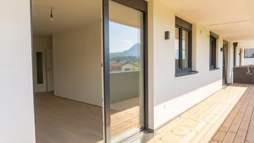 Langer Balkon mit Holzboden und Schiebetür zum Innenbereich, mit Bergblick im Hintergrund.