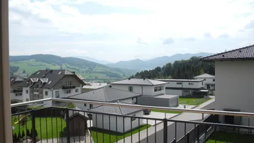 Blick vom Balkon auf die umliegende Wohnsiedlung und die grünen Berge in der Ferne.