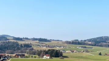 Panoramablick über eine ländliche Landschaft mit sanften grünen Hügeln und verstreuten Häusern.