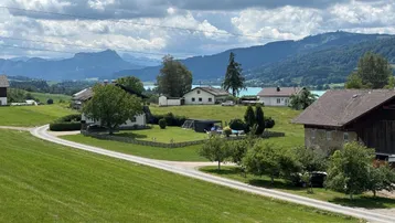Panoramablick über grüne Hügel, Häuser und einen See mit Bergen im Hintergrund.