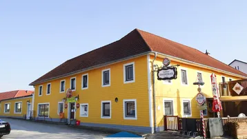 Gelbes Gasthausgebäude mit traditionellem roten Ziegeldach und mehreren Fenstern an einer Straße gelegen.