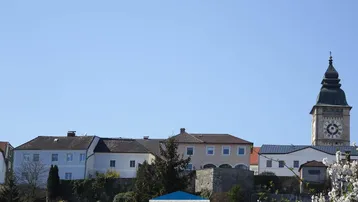 Blick auf eine historische Stadtansicht mit Kirchturm und umliegenden Gebäuden unter blauem Himmel.