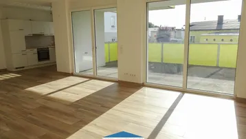 Heller offener Wohnbereich mit Holzboden und Blick auf die Küche sowie Zugang zum Balkon.